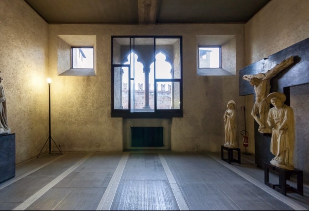 In VACUI Sala espositiva del Museo di Castelvecchio a Verona, con sculture in pietra e un grande finestrone centrale che mostra le mura medievali esterne. IN VACUI