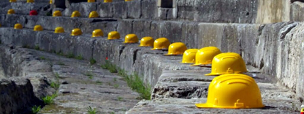 Sicurezza e lavoro: un'immagine simbolica quanto drammatica di una sfilata di caschi che non hanno protetto chi li indossava